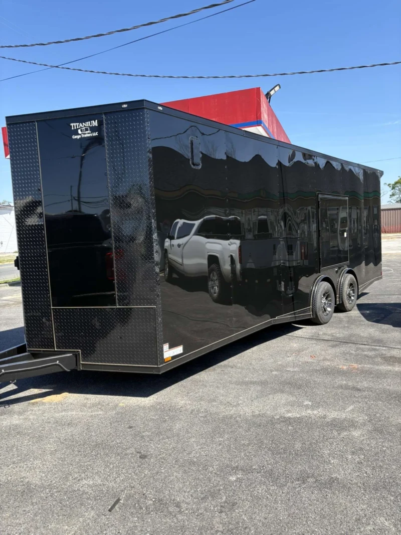 Large black enclosed cargo trailer with dual axles and side door, parked on pavement.