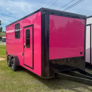 Bright pink enclosed cargo trailer with side door and dual axles, parked on grass.