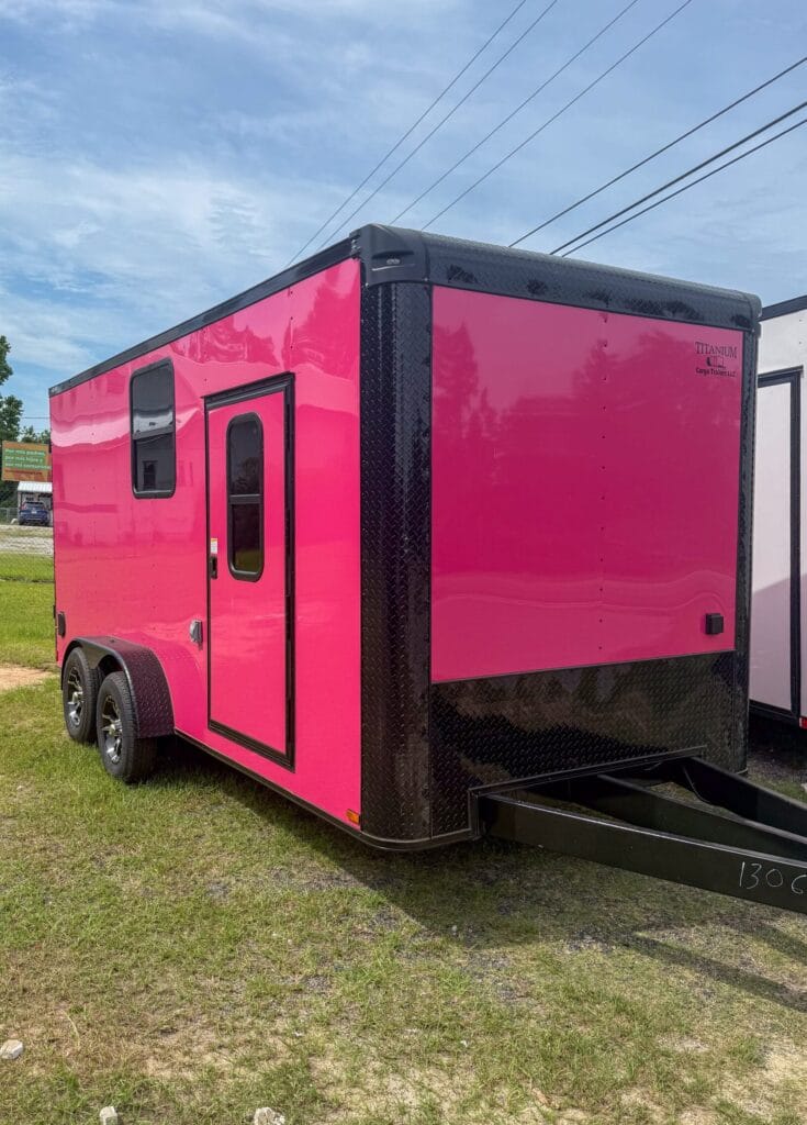 Bright pink enclosed cargo trailer with side door and dual axles, parked on grass.