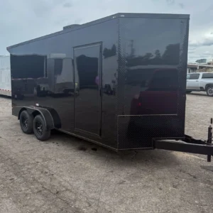 Black enclosed cargo trailer with side door and dual axles, parked on asphalt.
