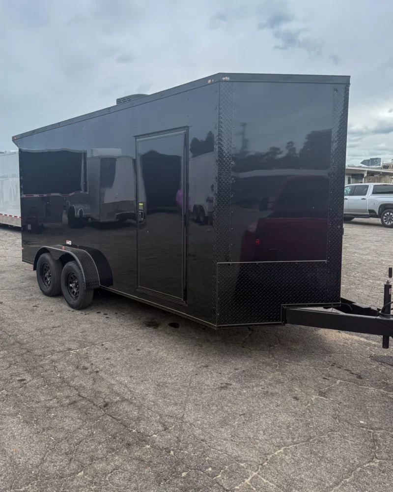 Black enclosed cargo trailer with side door and dual axles, parked on asphalt.