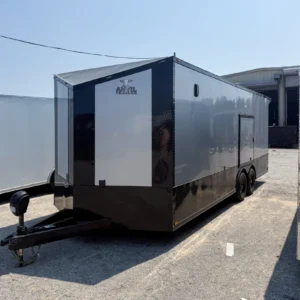 Black and gray enclosed dual-axle cargo trailer with side door, parked on pavement near buildings.