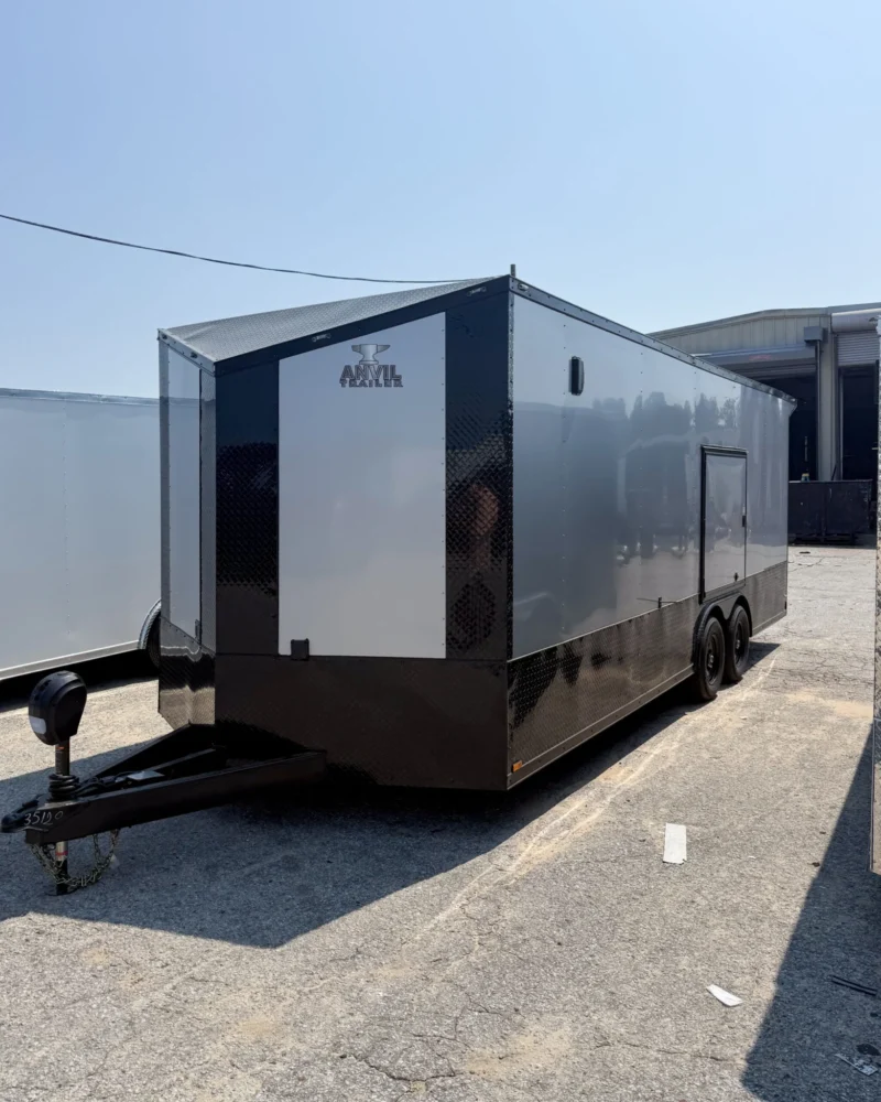 Black and gray enclosed dual-axle cargo trailer with side door, parked on pavement near buildings.
