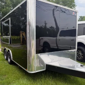 Black enclosed dual-axle cargo trailer with diamond plate trim, parked on grass beside a white pickup truck